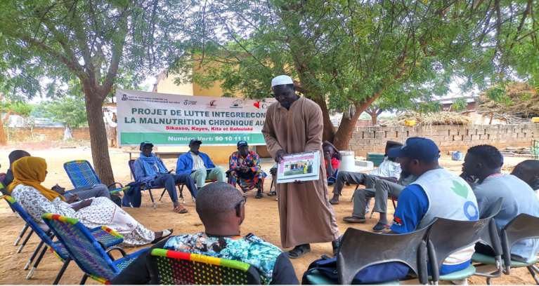 Un homme montre une photographie à un groupe de personnes assises en cercle.  