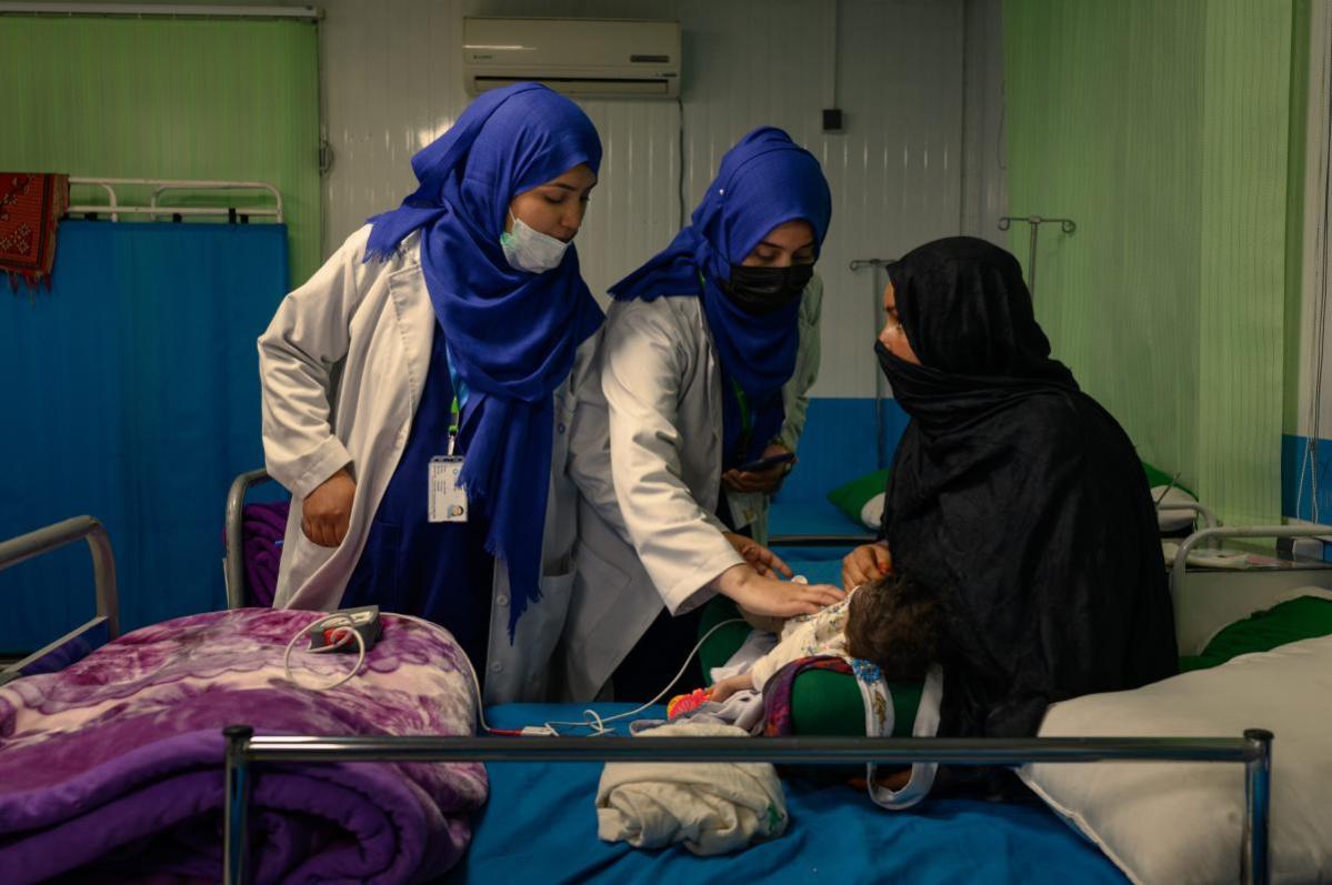 Enfermeras comprueban las constantes vitales de una niña de un mes y medio que padece desnutrición aguda grave y neumonía, tumbada sobre su abuela en una sala de hospitalización de la unidad de alimentación terapéutica de Acción contra el Hambre en la zona de Ahmad Shah Baba Mina de Kabul el 15 de abril de 2023